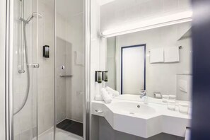 Een moderne badkamer met een douche met glazen wand, een witte wastafel met spiegel en een handdoekrek.