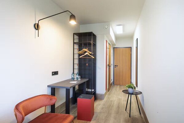Ein modernes Zimmer mit Schreibtisch, Stuhl, Kleiderhaken und einem Tisch mit einer Pflanze.