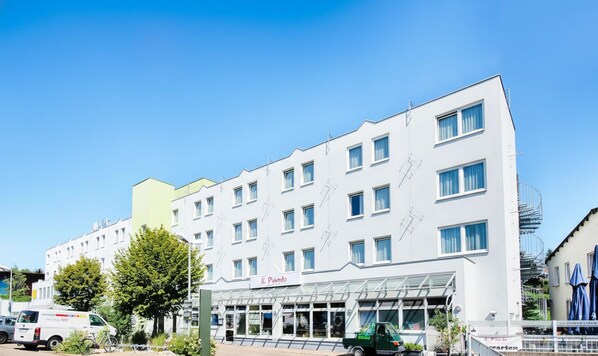 Ein modernes Hotel mit weißer Fassade, zahlreichen Fenstern und einem überdachten Eingangsbereich.