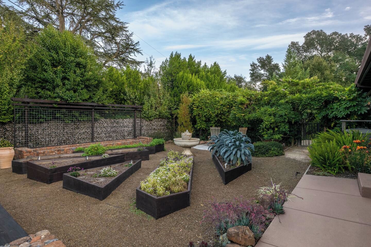 Un jardín con camas elevadas, un muro de piedra y diversas plantas.