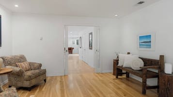 Een gang met een gestreept bankje, een houten zitting en een deur naar een andere kamer.