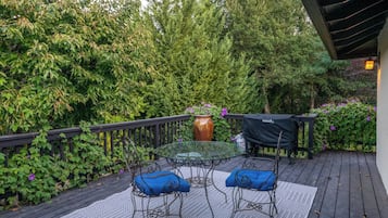 Eine Terrasse mit einem Glastisch und Stühlen, umgeben von üppigem Grün.
