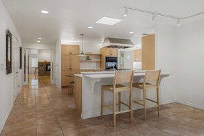 A modern kitchen with a central island, wooden chairs, and a built-in oven.