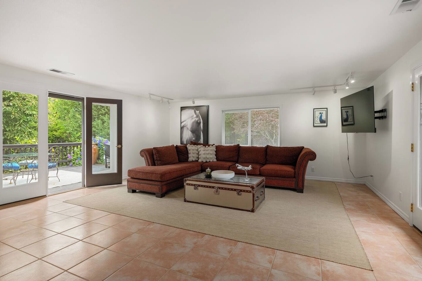 Una sala con un sofá modular, una mesa de centro y una maleta. Hay un ventanal corredera que da a un espacio exterior con terraza.