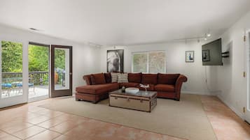 Una sala con un sofá modular, una mesa de centro y una maleta. Hay un ventanal corredera que da a un espacio exterior con terraza.