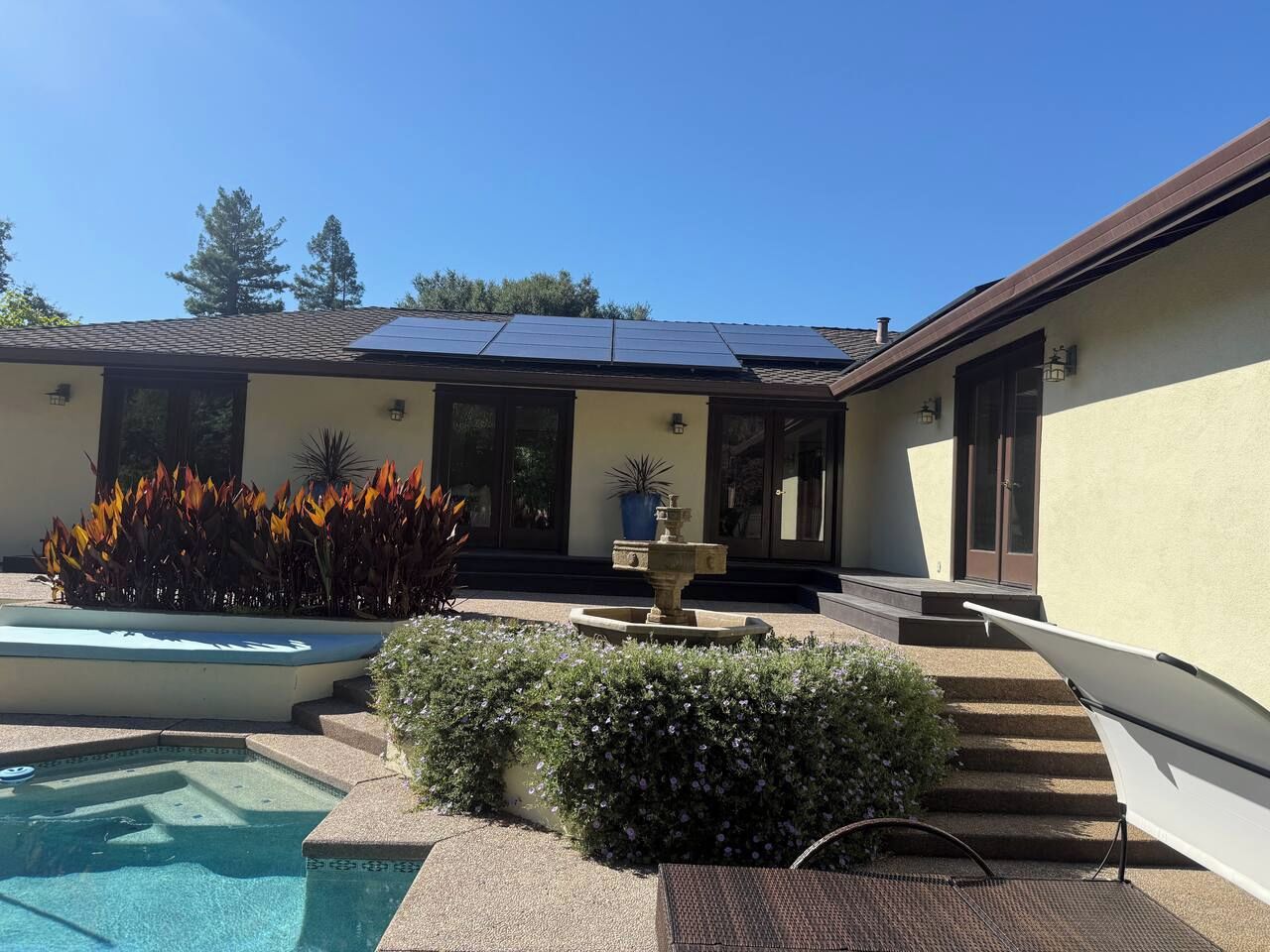 A residential property with a swimming pool, solar panels, a fountain, and a well-maintained garden.