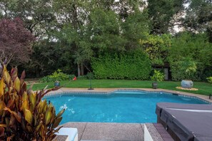 Une piscine entourée d’un jardin et dotée d’un espace salon abrité.