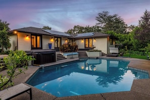 A modern house with a swimming pool, outdoor lighting, and a hot tub.