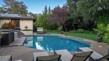 A swimming pool with lounge chairs and a hot tub in a landscaped backyard.