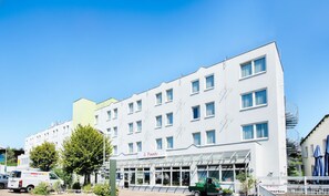 Ein modernes Hotel mit weißer Fassade, zahlreichen Fenstern und einem überdachten Eingangsbereich.