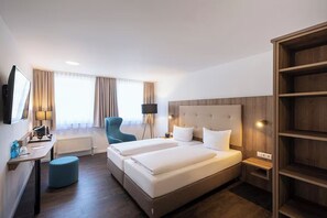 Ein Hotelzimmer mit einem Bett, einem Schreibtisch, einem Stuhl, einer Lampe und einem Bücherregal.