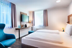 Ein Hotelzimmer mit Bett, Schreibtisch, Sessel, Fernseher und einem Fenster mit Vorhängen.