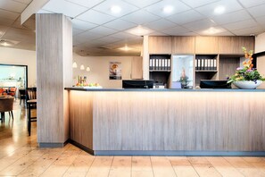 Ein moderner Empfangsbereich mit einem Holzbüro, einer großen Pflanze im Topf und einer Sitzecke mit Stühlen und Tischen.