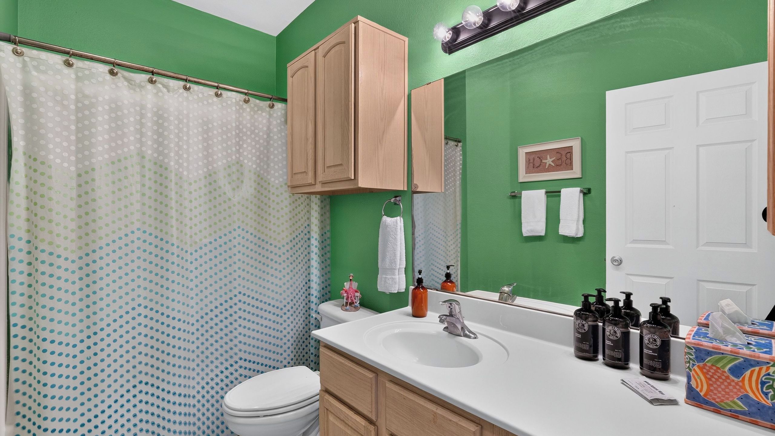 A bathroom with a green wall, a white sink, a toilet, and a shower curtain with a polka dot pattern.