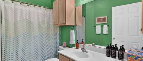 A bathroom with a green wall, a white sink, a toilet, and a shower curtain with a polka dot pattern.