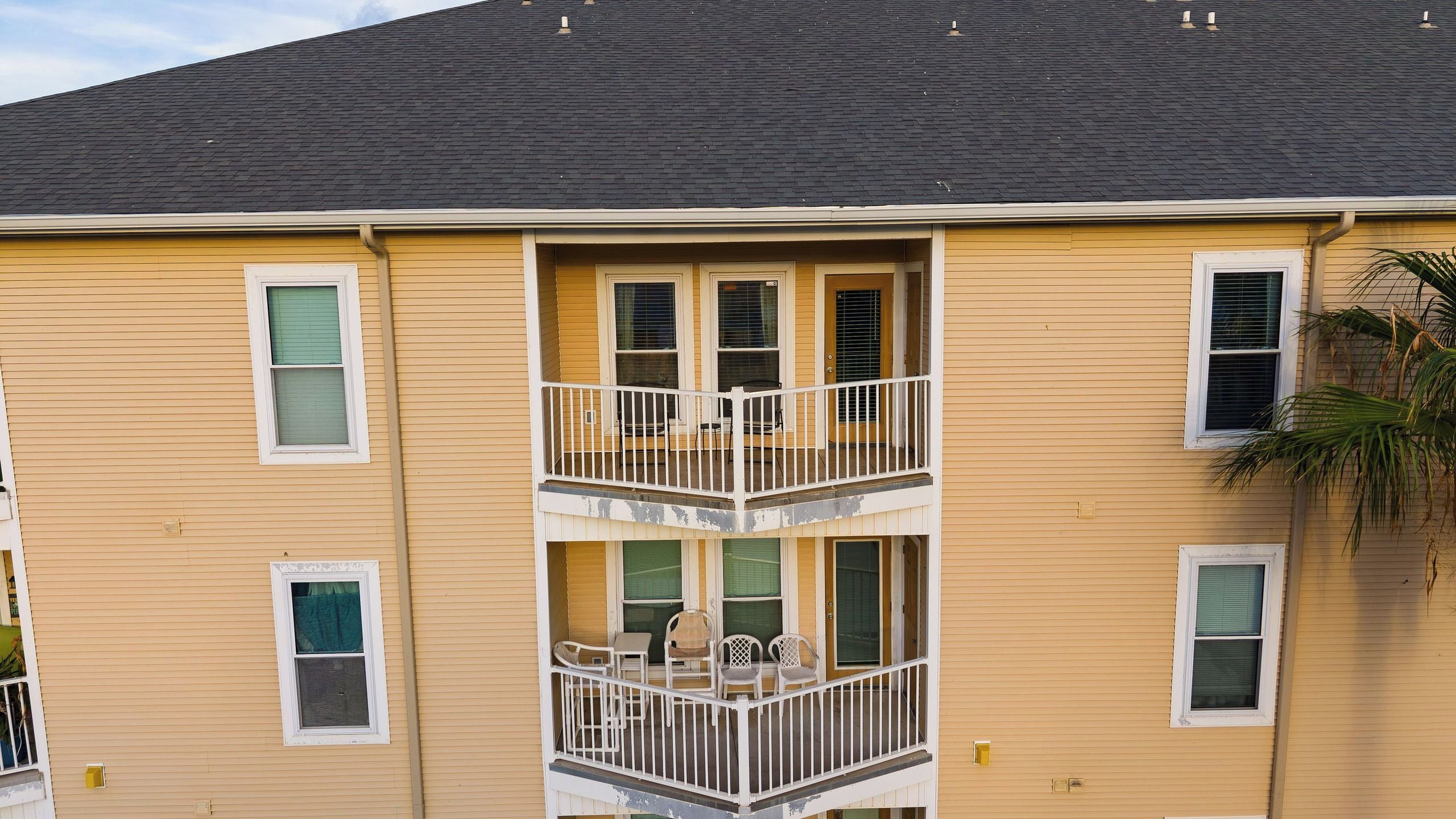 A multi-story building with a balcony on the second floor, featuring a small table and chairs.