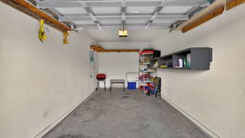 A garage with a concrete floor, a red toolbox, a blue trash bin, and a metal bench.