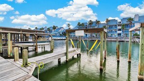 A wooden dock extending into calm water, with a boat docked on the left. - Paradise Found by Avantstay Waterfront Retreat Private Boat Slip + Shared Pool North Padre (Corpus Christi)