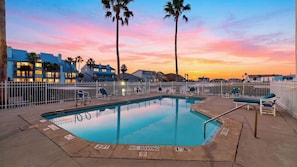 A swimming pool with a white fence, lounge chairs, and palm trees. - Paradise Found by Avantstay Waterfront Retreat Private Boat Slip + Shared Pool North Padre (Corpus Christi)