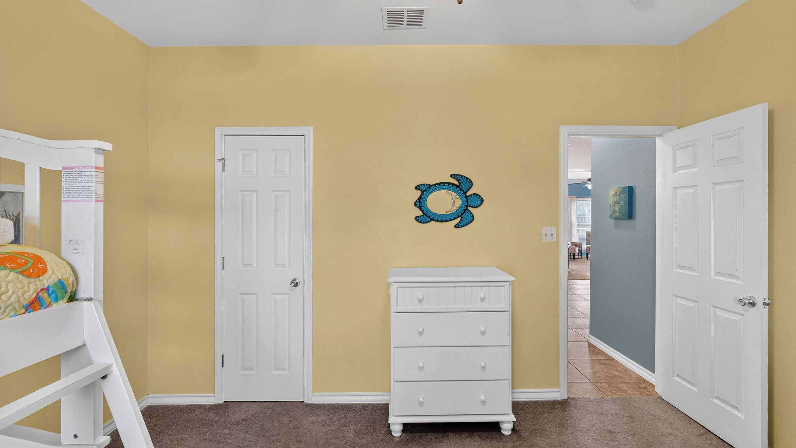 A hallway with beige walls, white doors, a white dresser, and a blue turtle wall decoration.
