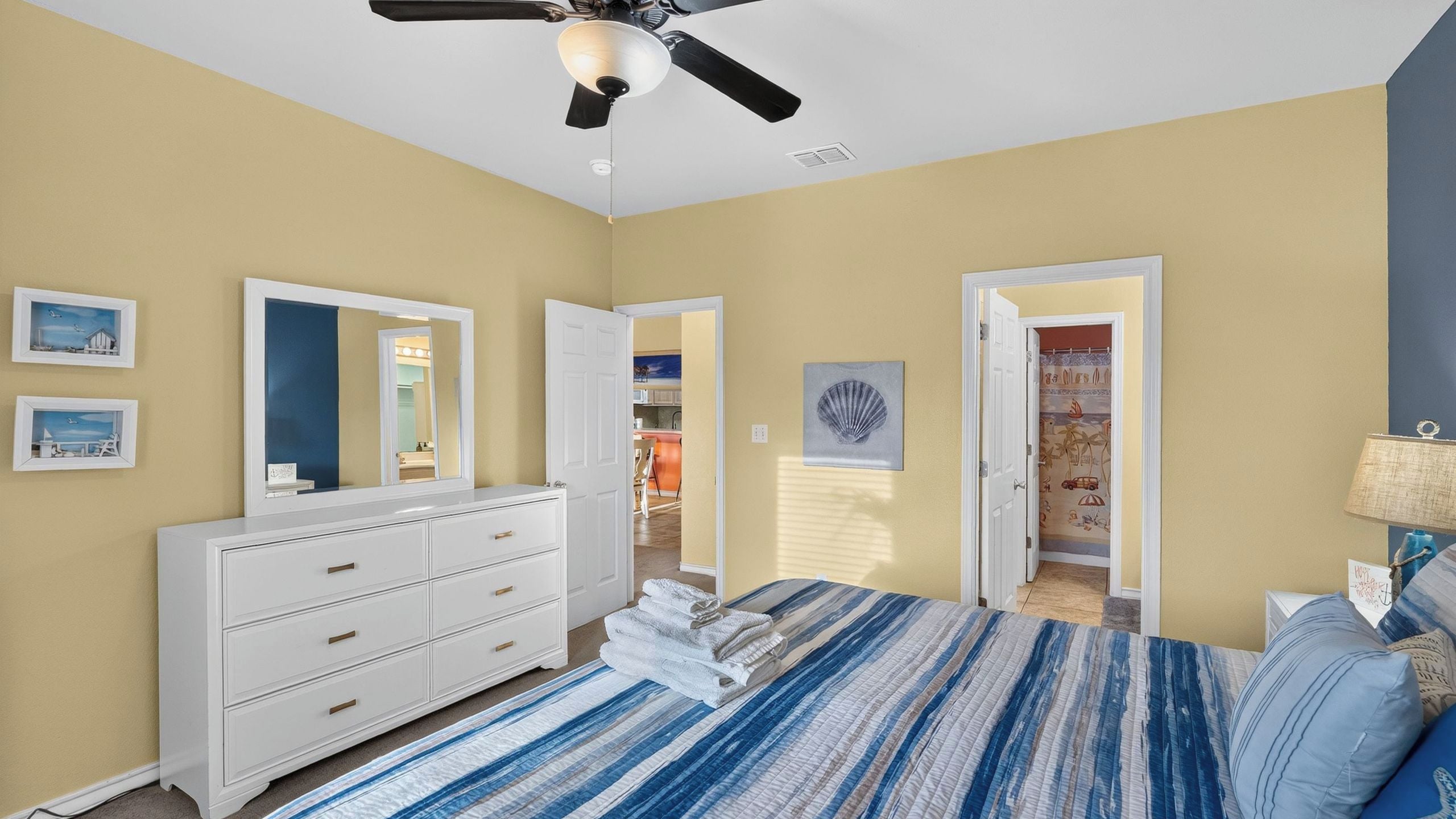 A bedroom with a bed, dresser, and a ceiling fan. There are doors leading to other rooms.