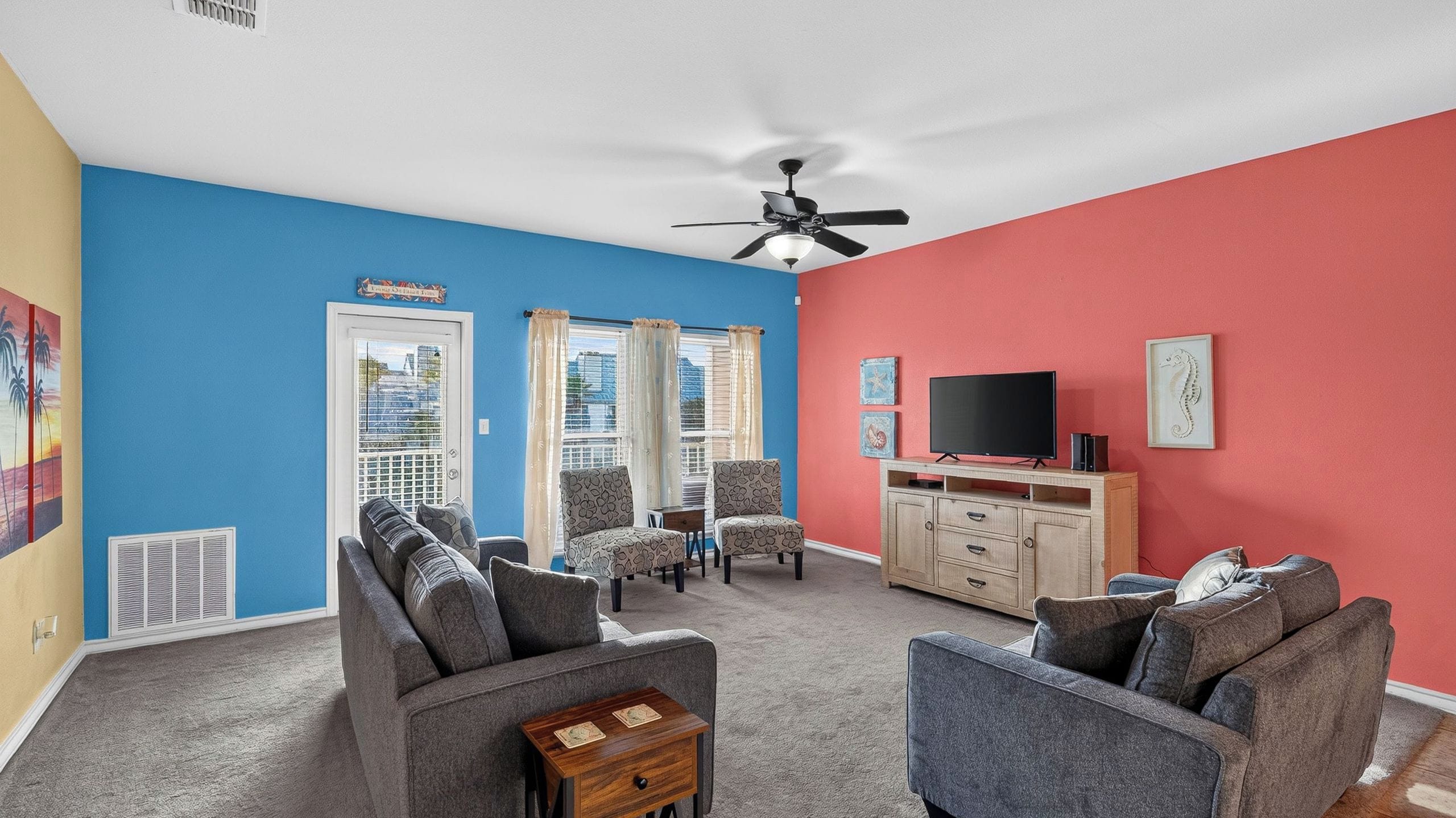 A living room with a blue and red wall, a ceiling fan, a TV, and a cabinet.
