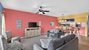 A living room with a flat-screen TV, a ceiling fan, and a dining area with a kitchen in the background. - Paradise Found by Avantstay Waterfront Retreat Private Boat Slip + Shared Pool North Padre (Corpus Christi)