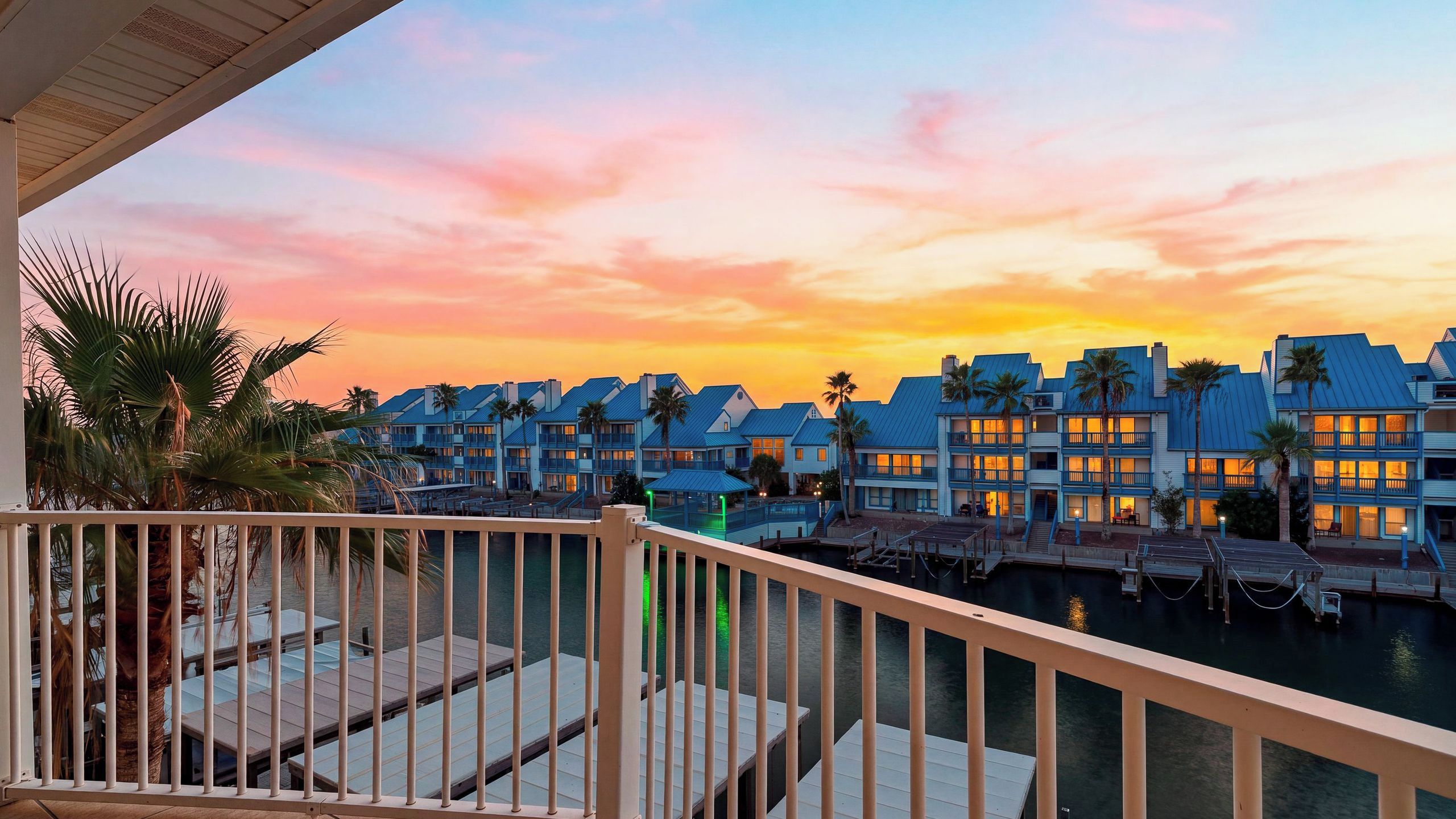 A waterfront hotel with multiple buildings, a pool area, and a sunset view.