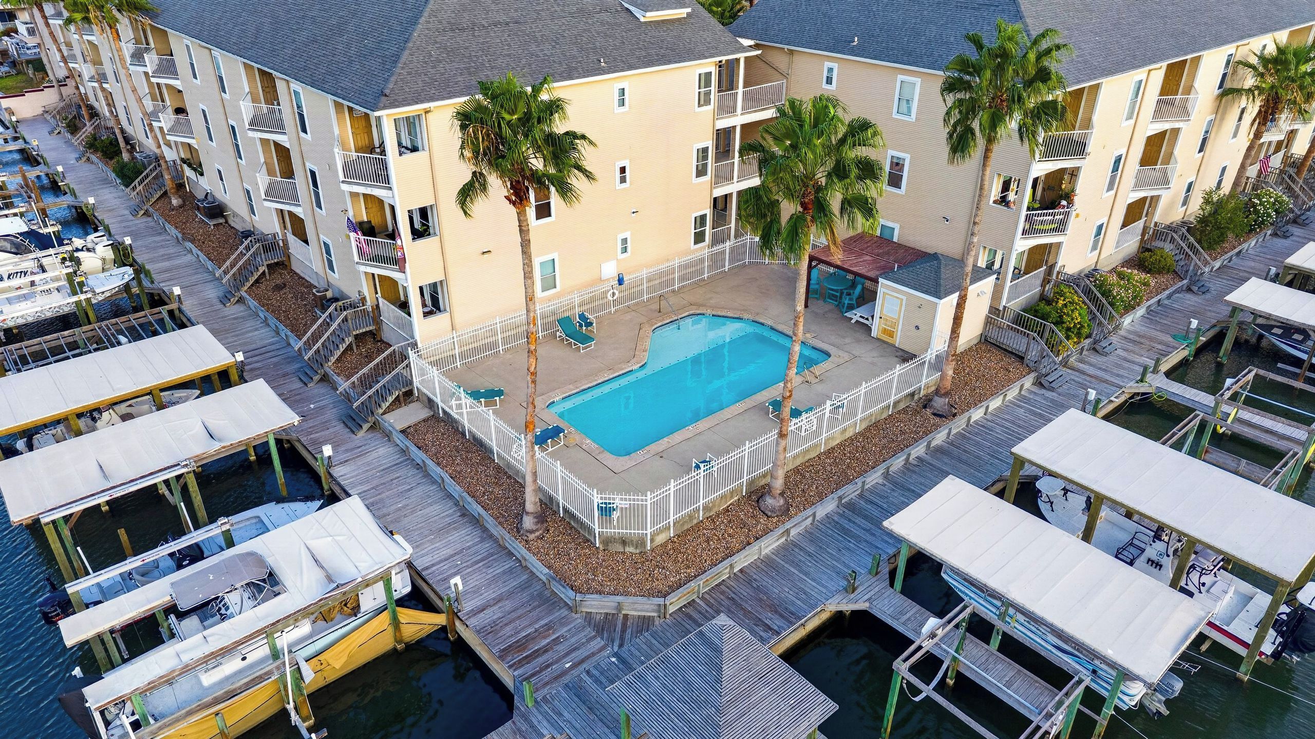 A multi-story hotel with a swimming pool, outdoor seating, and docked boats.
