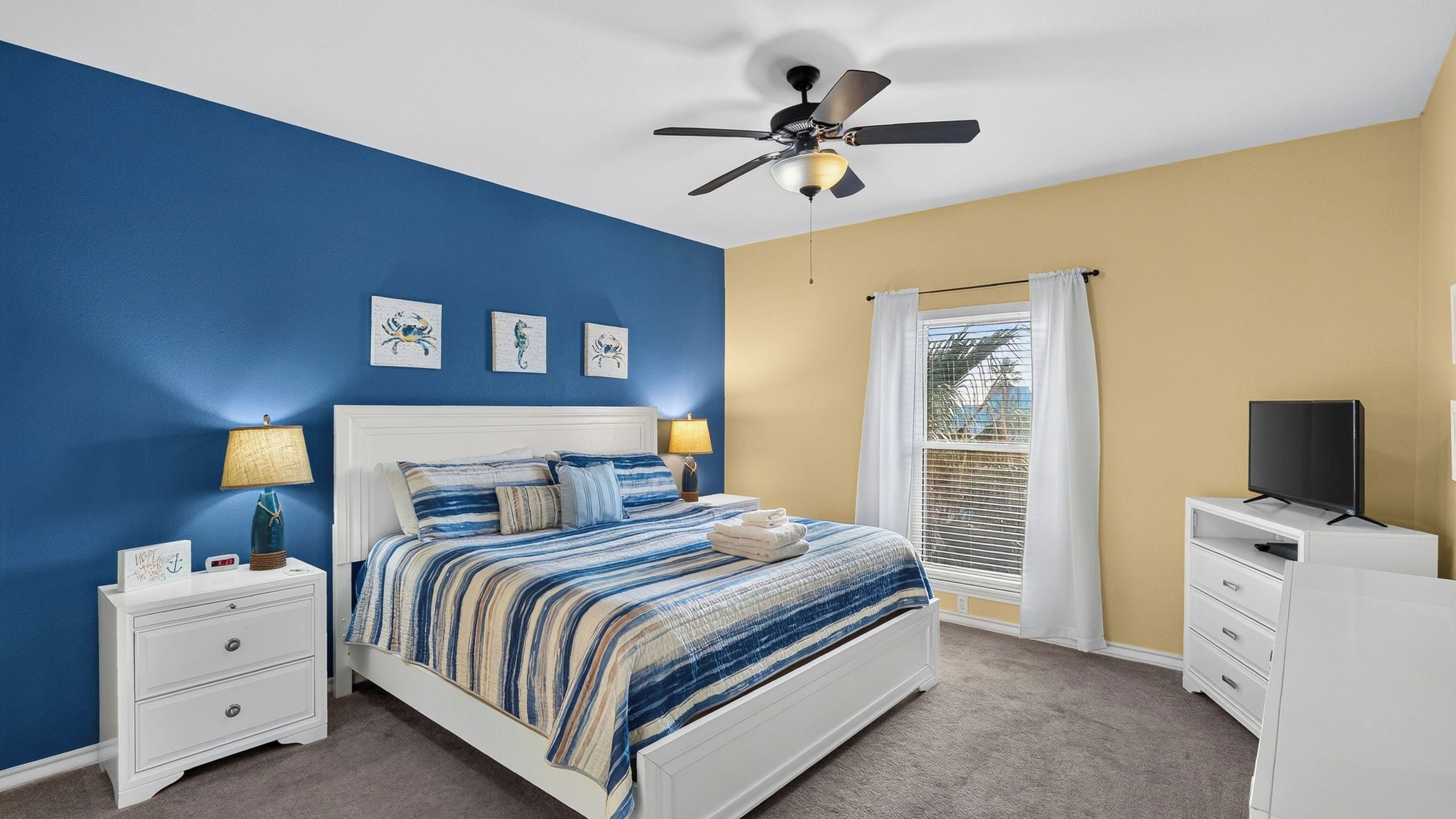 A bedroom with a bed, nightstands, a ceiling fan, a window with curtains, and a TV stand.