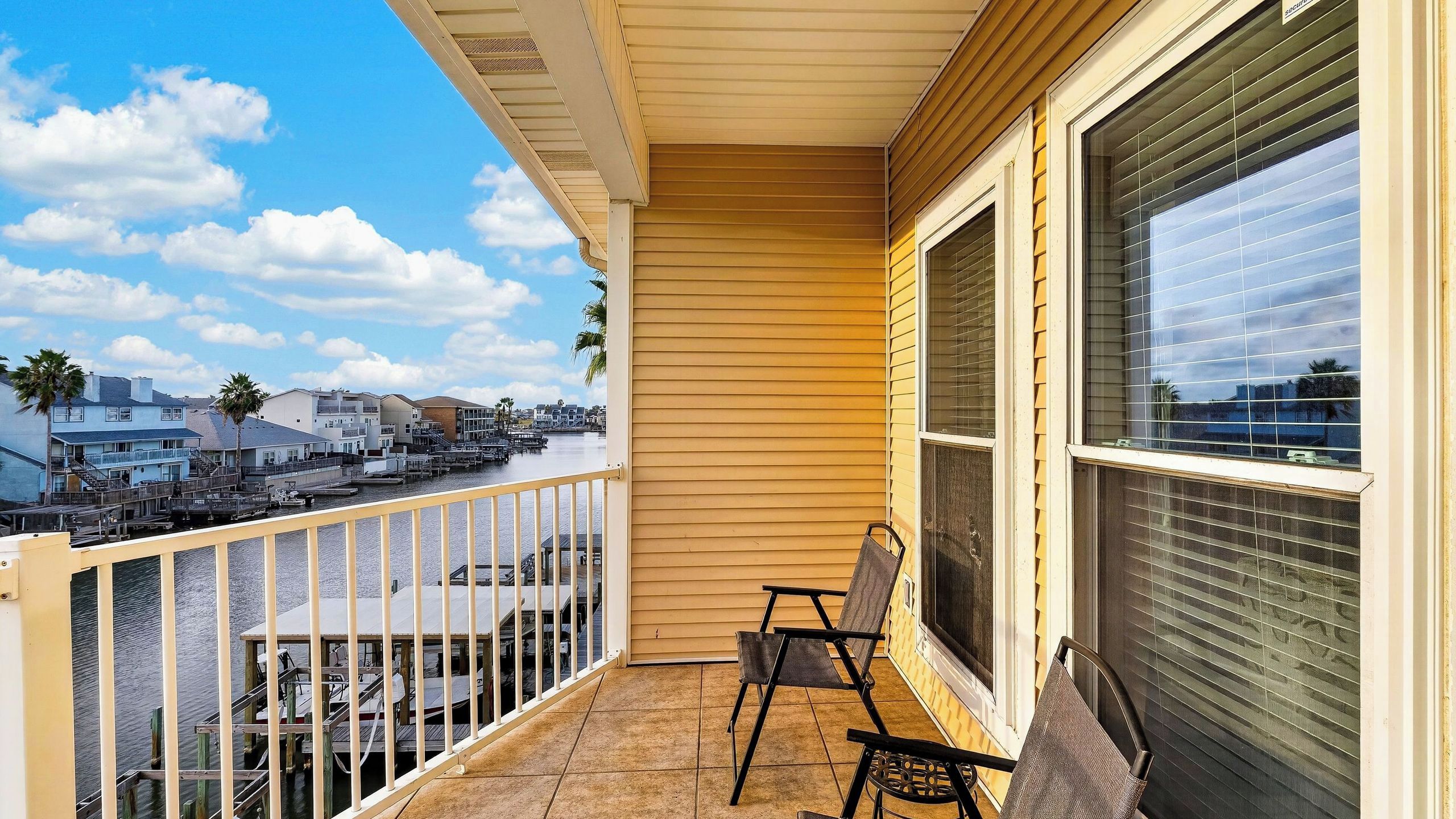 A balcony with a view of a marina, a chair, and a large window with blinds.