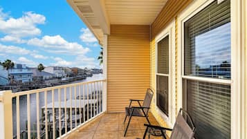 A balcony with a view of a marina, a chair, and a large window with blinds.