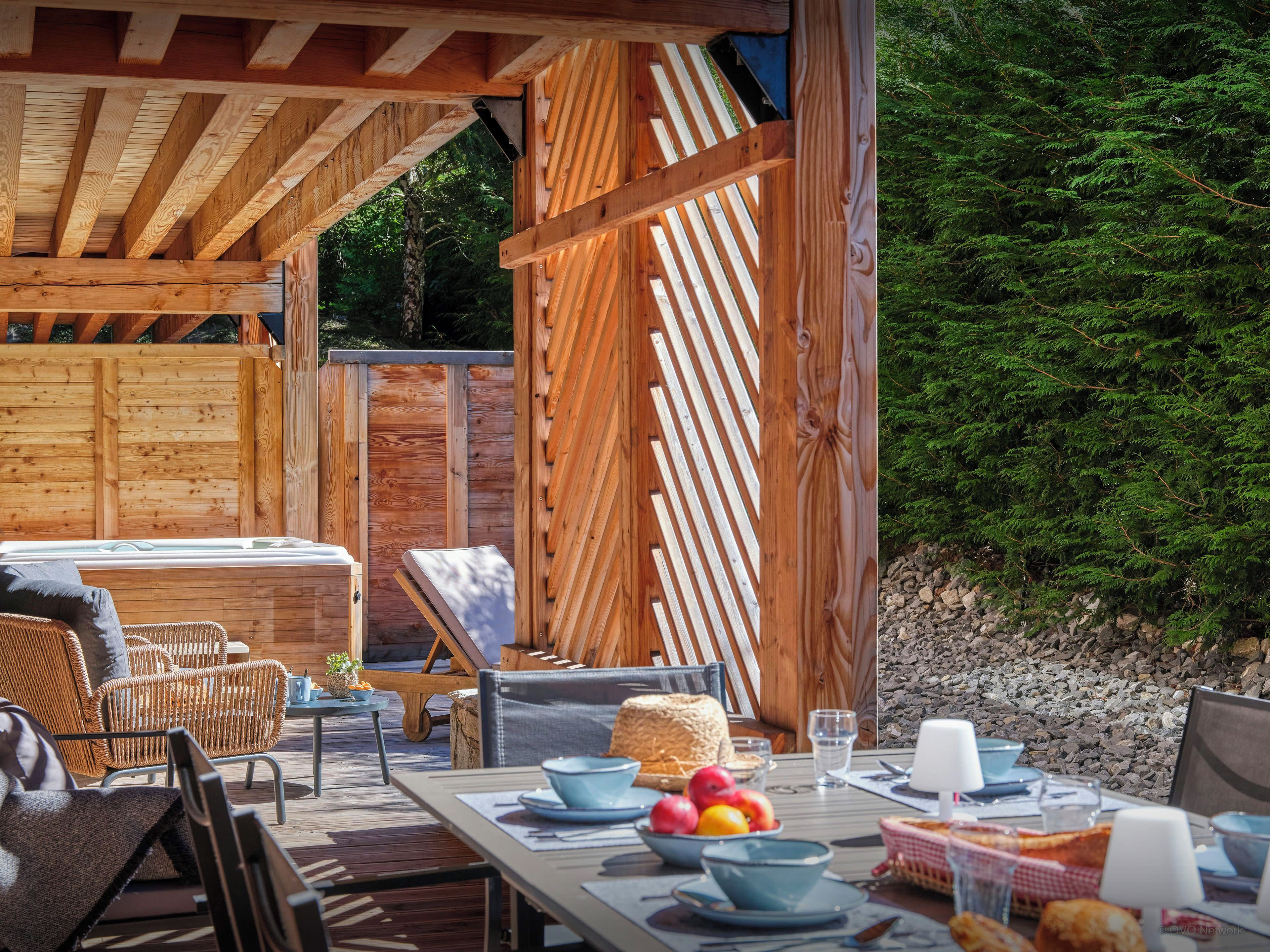 An outdoor wooden deck with wicker furniture, a hot tub, and a dining table set with plates, bowls, and glasses.