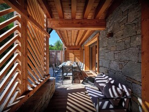 A covered outdoor dining area with a stone wall, wooden beams, and a table set for dining. - Lodge Ubuntu - modern apartment with a hot tub - OVO Network (Châtel)