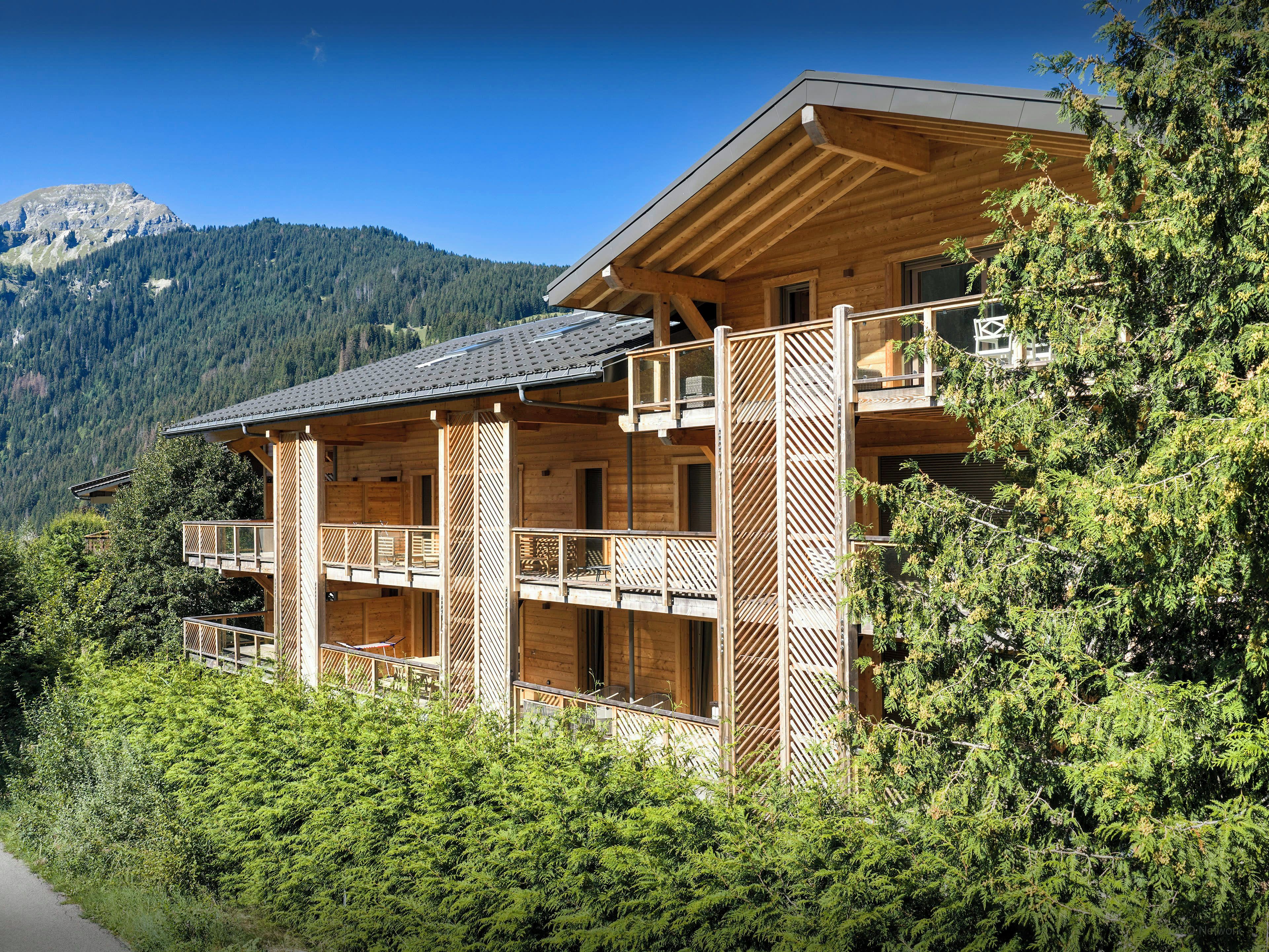 Eine Holzchalet mit mehreren Balkonen vor einer Bergkulisse.
