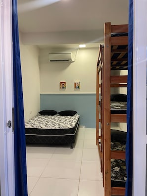 Quarto com cama, beliche, ar condicionado e prateleira na parede.