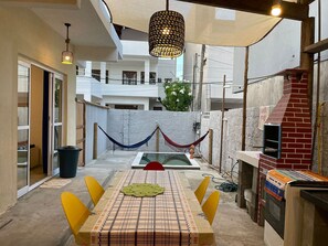 Un espacio exterior para comer con una mesa, sillas, una hamaca y un horno de ladrillo.