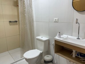 Un baño con inodoro, cortina de ducha, lavabo y un mueble de madera.