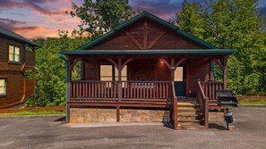 A wooden cabin with a porch, stone foundation, and a grill outside. - Hot Tub, Fireplace, Game Room, 2 Mi To Town (Gatlinburg)