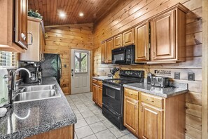 A kitchen with wooden cabinets, a stainless steel sink, a black stove, and a microwave. - Hot Tub, Fireplace, Game Room, 2 Mi To Town (Gatlinburg)