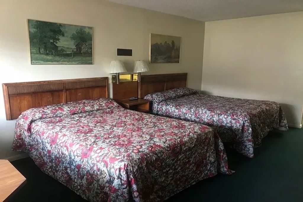 Een hotelkamer met twee bedden, een houten hoofdbord, een nachtkastje met lampen en twee schilderijen aan de muur.