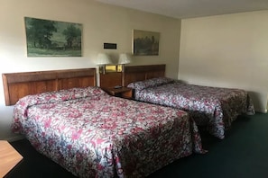 Habitació d'hotel amb dos llits, un panell de fusta al capçal, una tauleta de nit amb làmpades i dos quadres penjats a la paret.