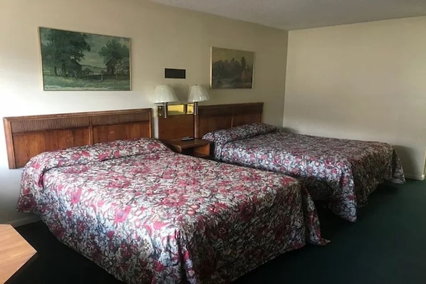 A hotel room with two beds, a wooden headboard, a nightstand with lamps, and two wall-mounted paintings.