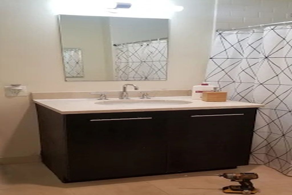 Een badkamer met een wastafel, spiegel en een douchegordijn met een geometrisch patroon.
