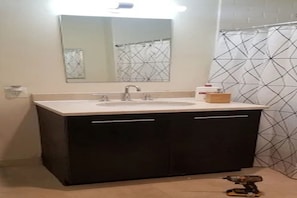 Un baño con lavamanos, espejo y cortina de ducha con diseño geométrico.