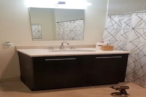 Un baño con lavamanos, espejo y cortina de ducha con diseño geométrico.
