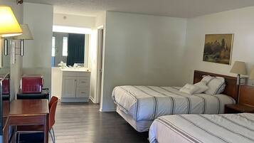 A hotel room with two beds, a desk, a chair, a small table, a lamp, and a painting on the wall.