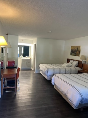 A hotel room with two beds, a desk, a chair, a small table, a lamp, and a painting on the wall.