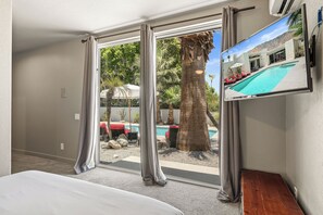 Habitació d'hotel amb una gran porta corredissa de vidre que dona a una zona de piscina, un llit i un televisor fixat a la paret.
