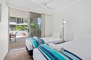 A hotel room with two beds, a ceiling fan, a sliding glass door leading to a balcony, and a small table with chairs outside. - Sandown Right on Mermaid Beach (Gold Coast)